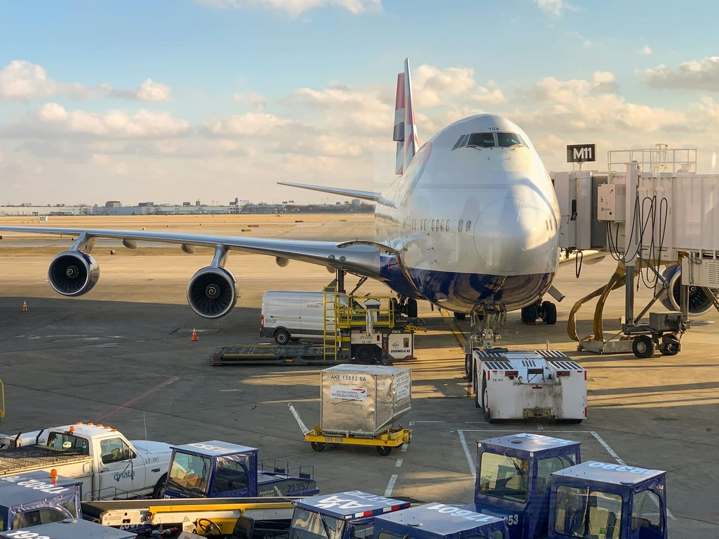 Large aircraft at an airport stand with cargo containers and ground vehicles in the foreground