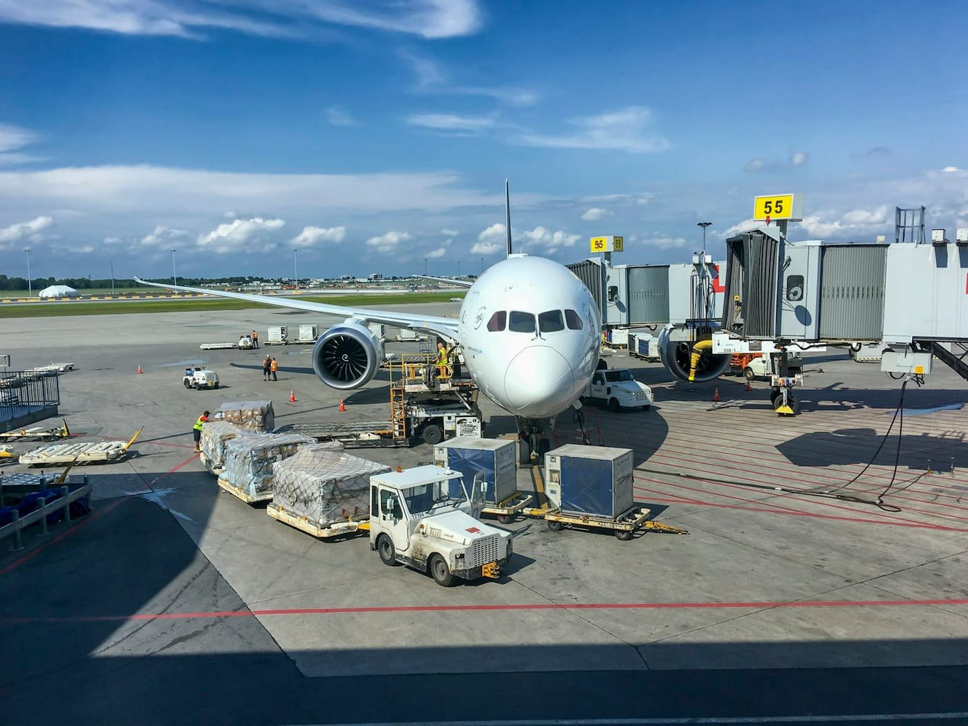 Aircraft at an airport gate with cargo containers and tugs on the apron