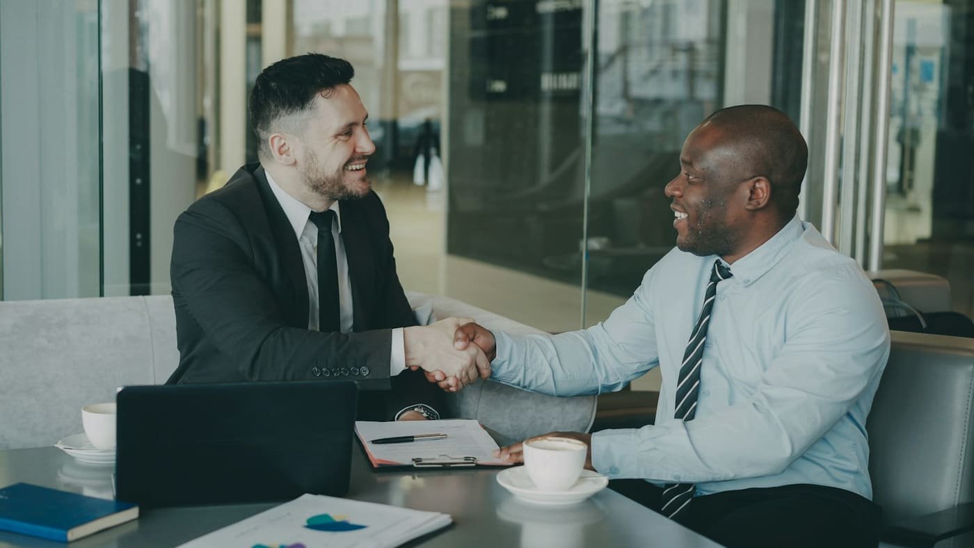Two businessmen shaking hands across a table in an office