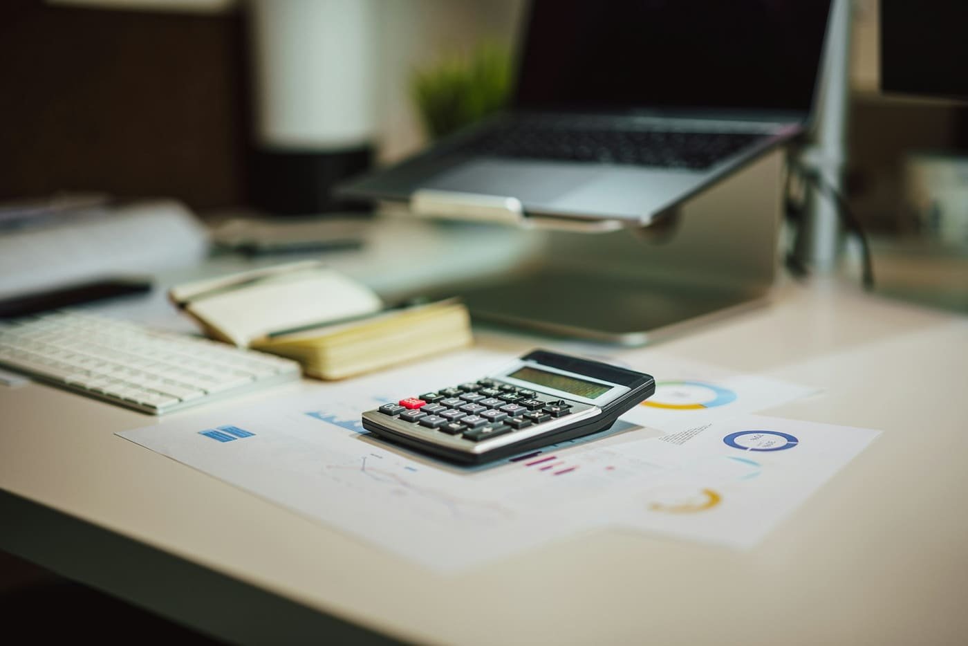 Calculator on a desk beside a laptop and printed charts