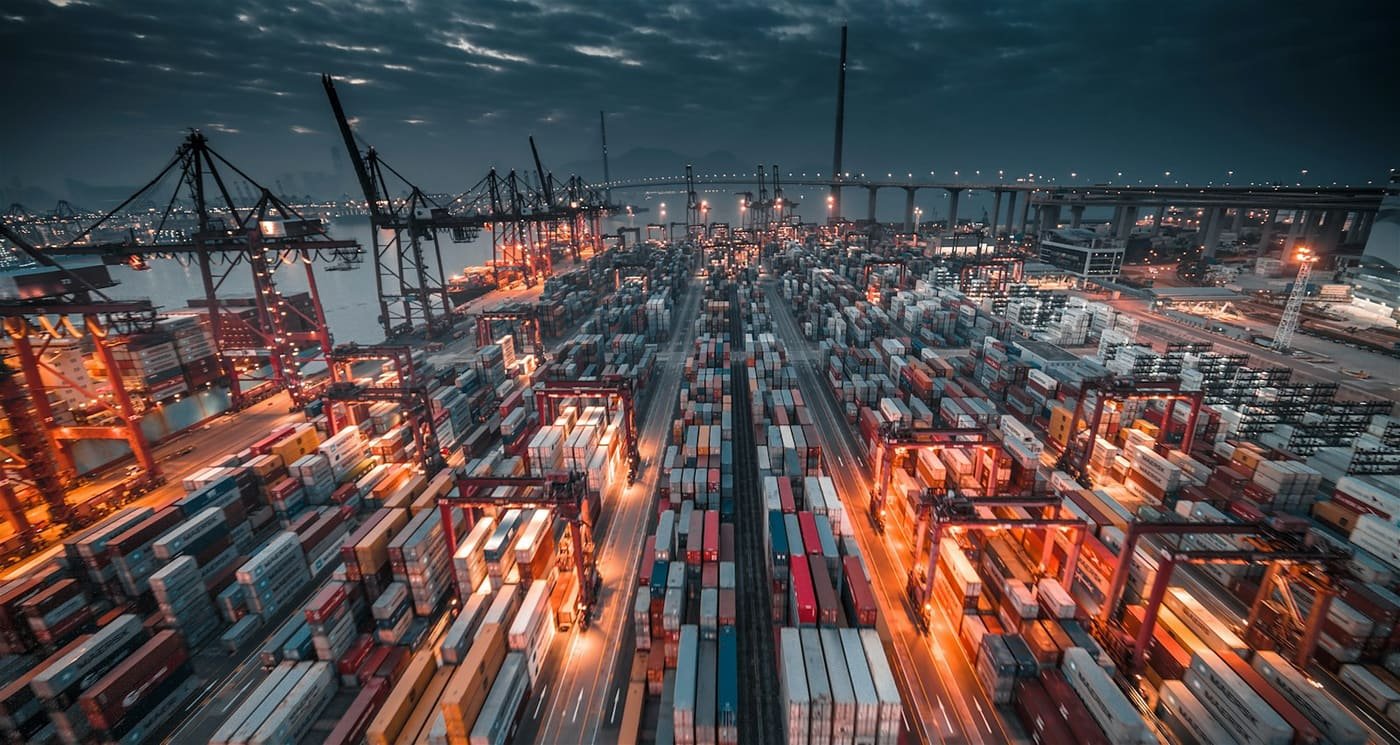 Container port at dusk with lit cranes and rows of stacked containers