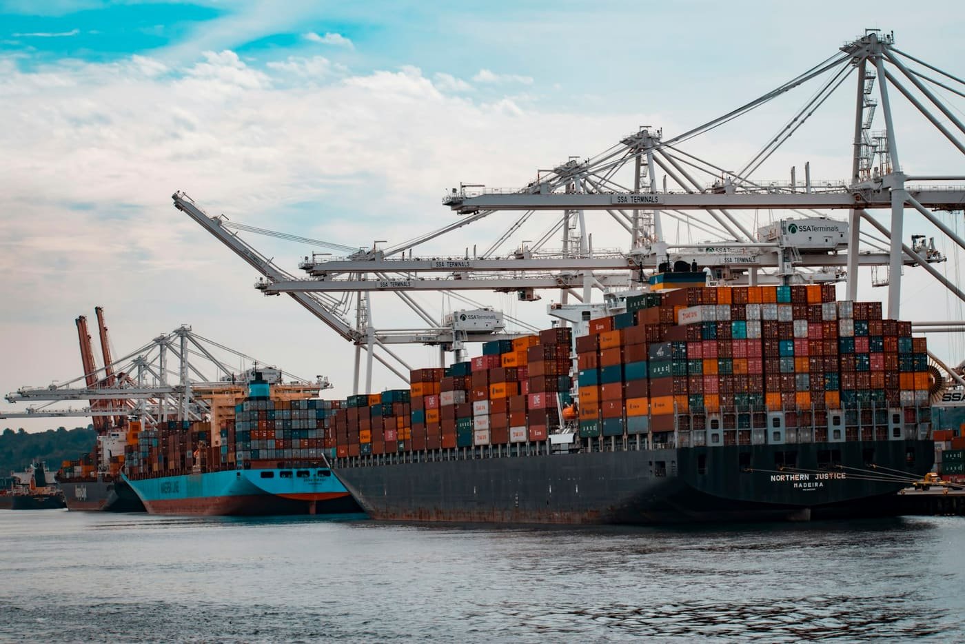 Container ships docked at a pier beneath quay cranes