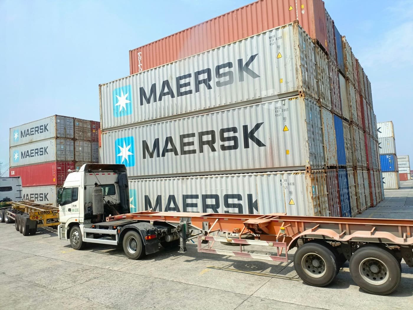 Container truck parked beside stacks of containers inside a port terminal