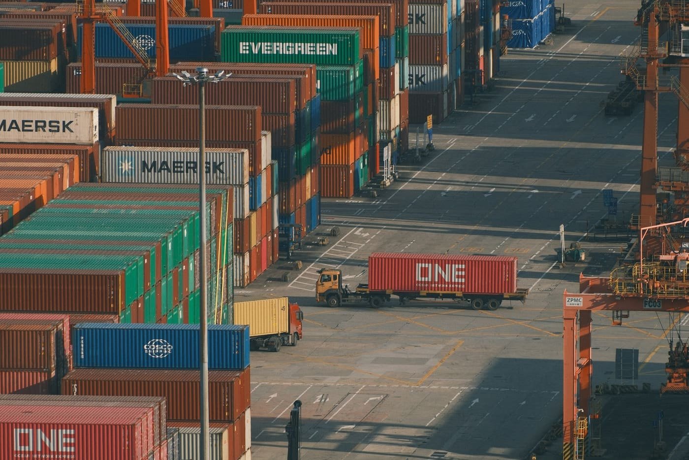 Container yard with stacks of colourful containers and a truck carrying a container along the aisle