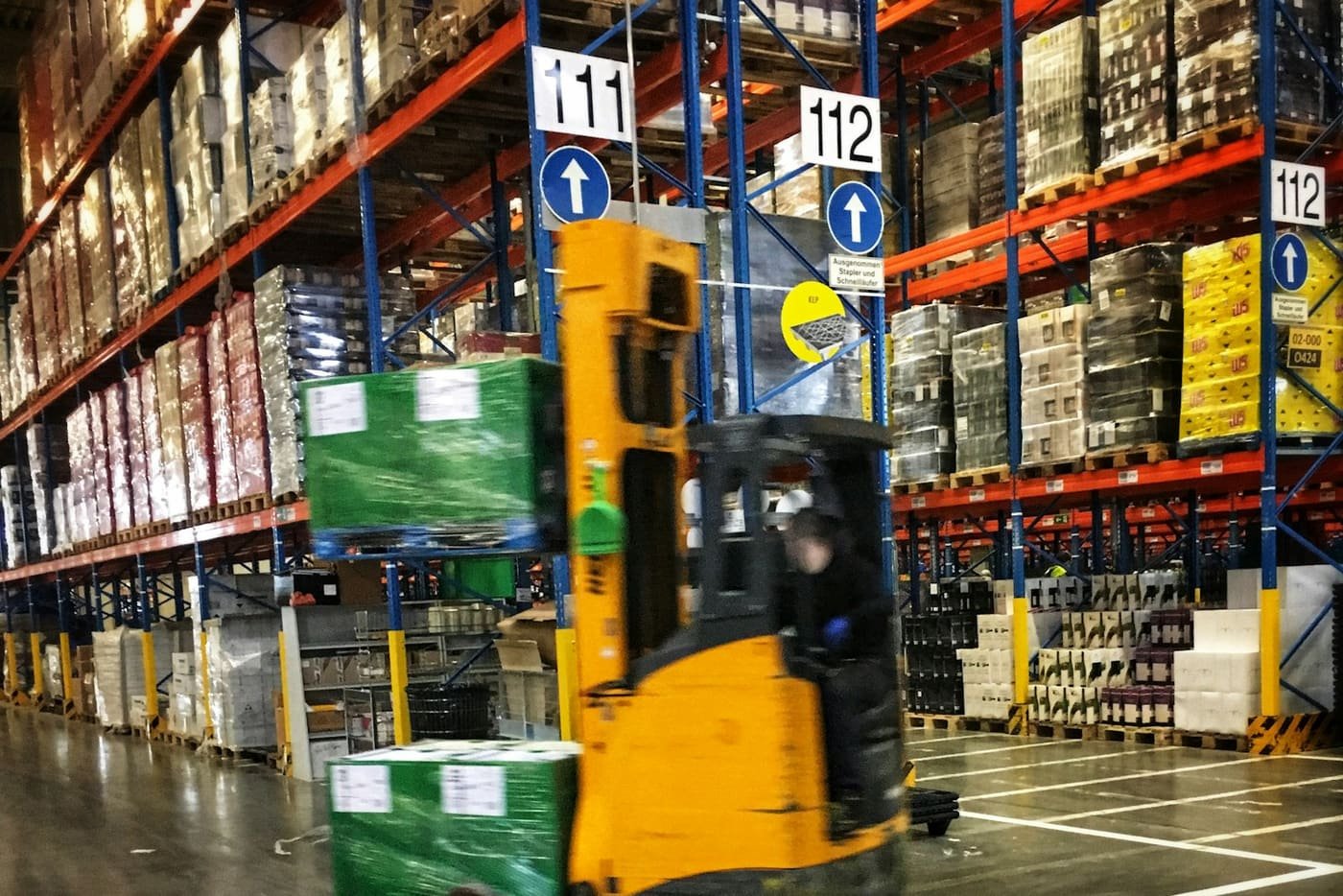 Forklift moving pallets between tall warehouse racking