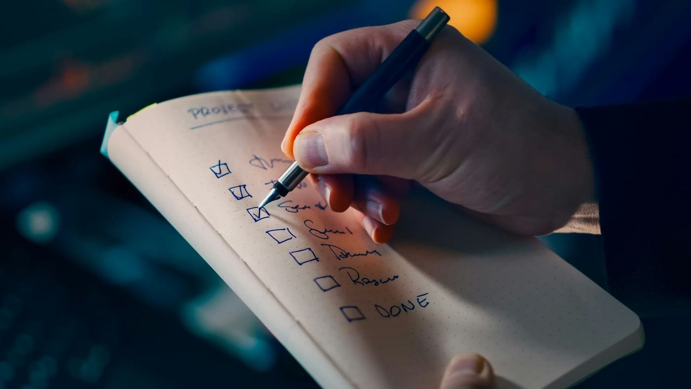 Hand ticking items off a handwritten checklist in a notebook