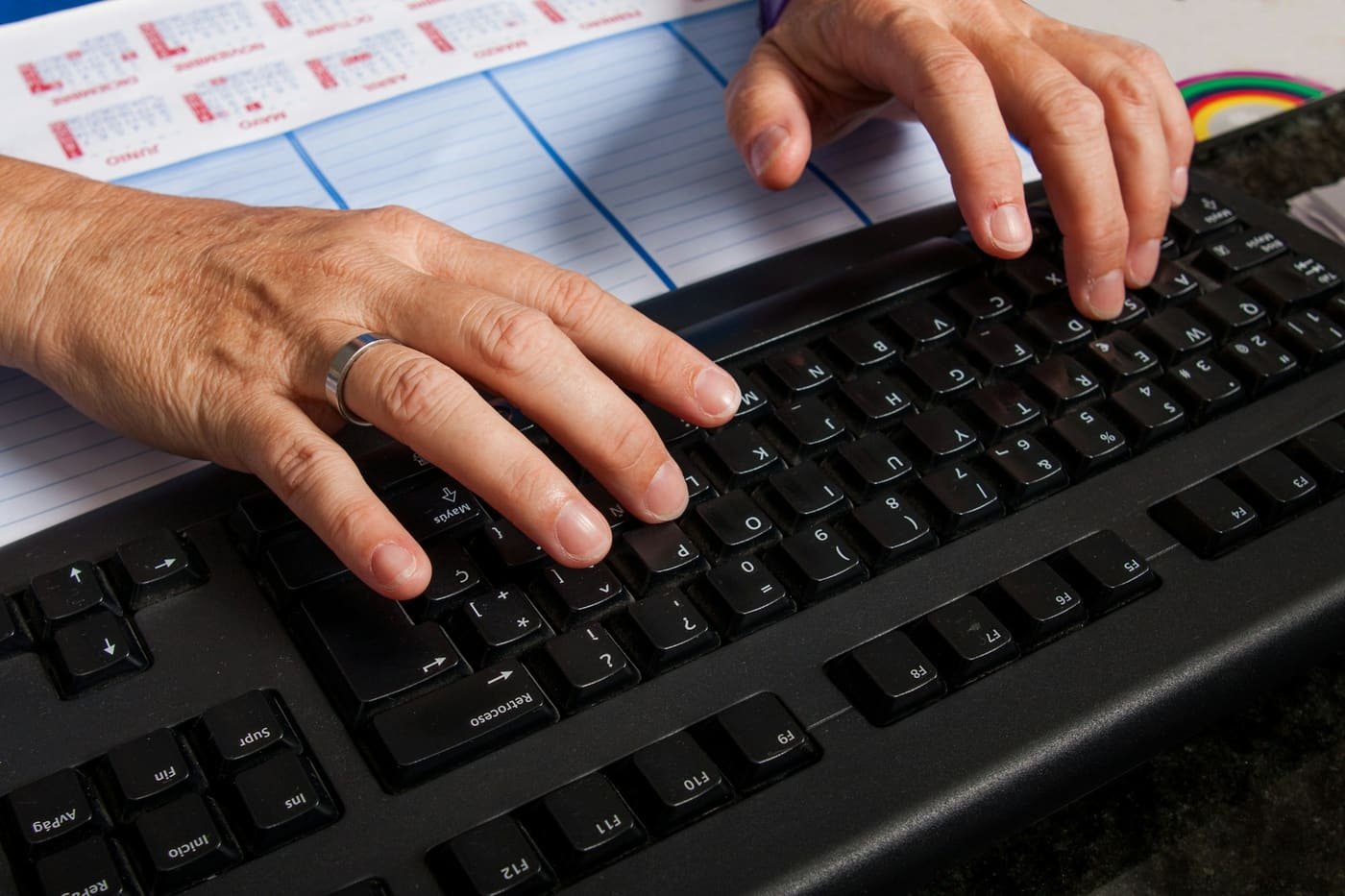 Close-up of a person's hands typing on a keyboard at a desk