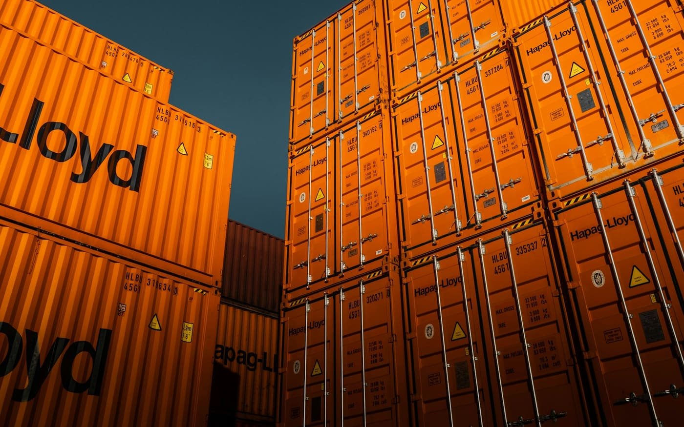 Stacked orange shipping containers against a deep blue sky
